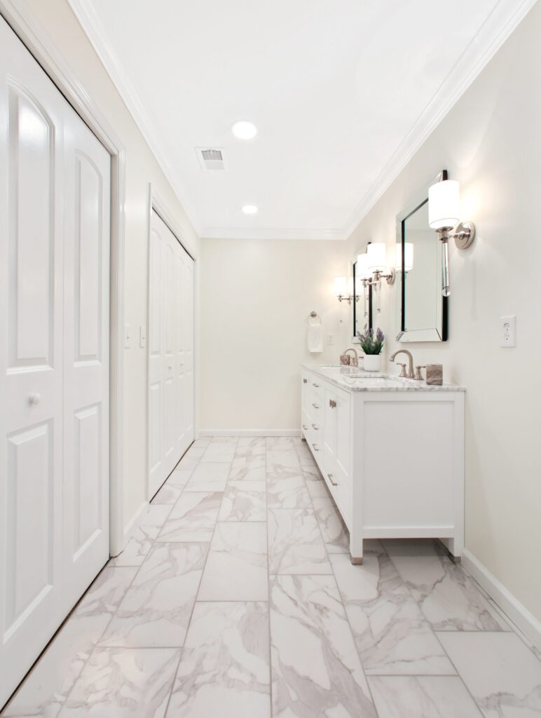 Modern bathroom remodel featuring white cabinetry, marble flooring, dual mirrors, and stylish lighting, enhancing functionality and comfort for a spa-like retreat in Cumming, GA.
