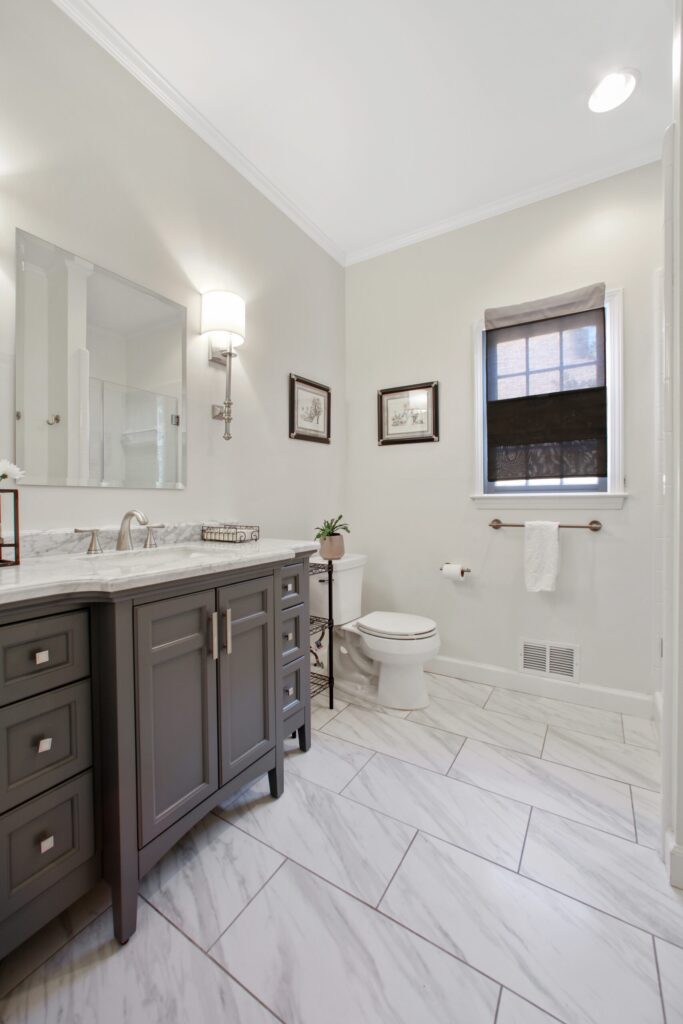 Modern bathroom remodel featuring a gray vanity with marble countertop, elegant lighting, and stylish tile flooring in a neutral color scheme, emphasizing functionality and comfort for enhanced daily living.