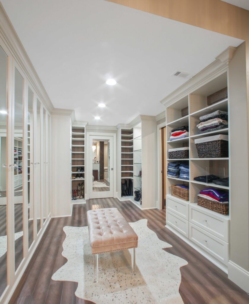 Stylish and organized basement closet with mirrored doors, shelving for clothing and accessories, a plush bench, and modern lighting, showcasing HomeVantage's home remodeling expertise.
