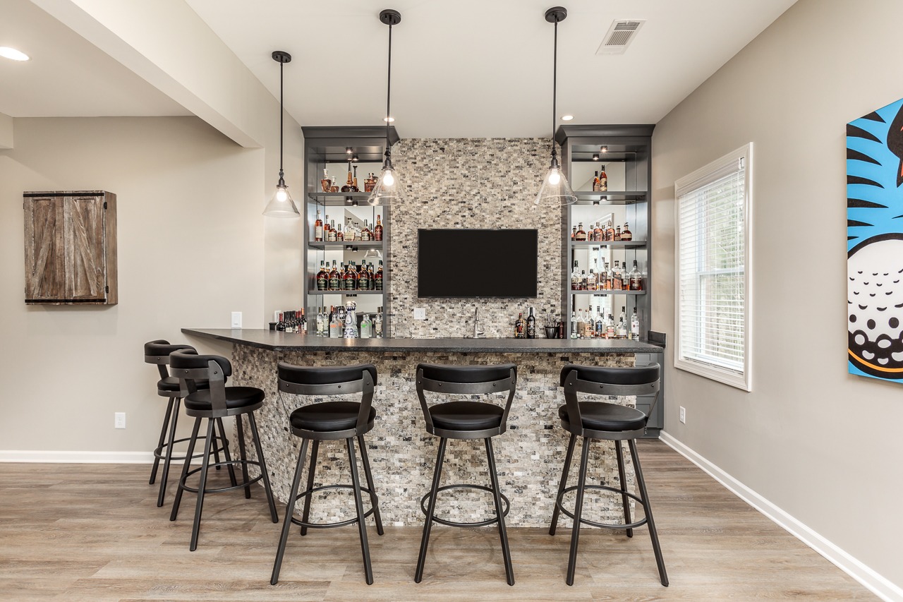 Modern basement bar with stylish cabinetry, stone backsplash, and seating, designed for entertaining and hosting gatherings.