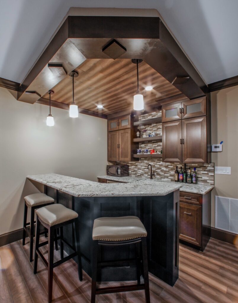 Basement bar area featuring granite countertop, dark wood cabinetry, stylish pendant lighting, and organized storage for bottles, designed for functional and aesthetic appeal in basement remodeling.