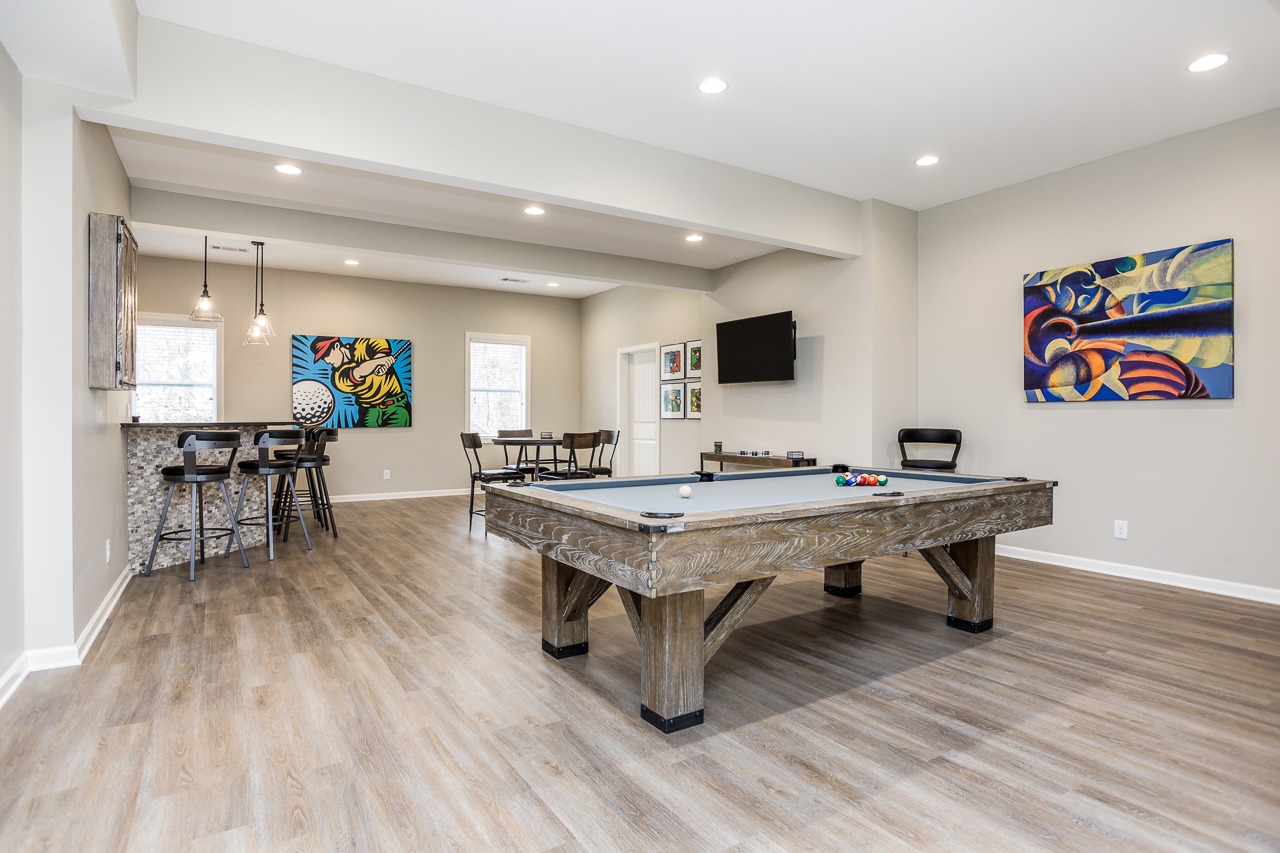 Modern basement recreation room featuring a billiard table, stylish bar seating, colorful wall art, and a television, showcasing a functional and inviting space for entertainment and relaxation.