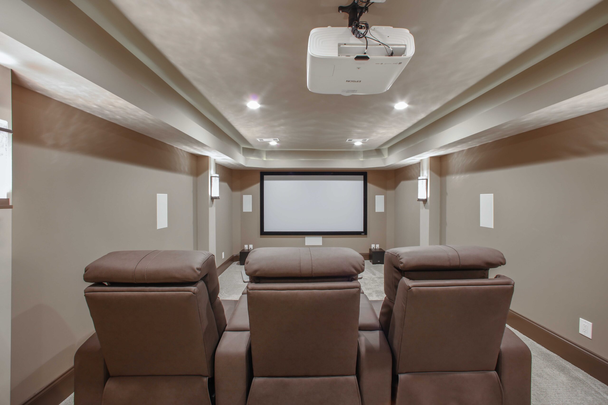 Home theater design featuring plush reclining chairs, a projector, and a large screen, emphasizing comfort and functionality for home expansion projects.