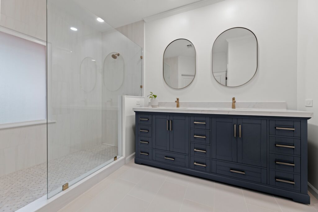 Modern bathroom design featuring a spacious shower with glass enclosure, dual round mirrors above a navy blue vanity with gold fixtures, and elegant tile flooring, showcasing high-quality craftsmanship by HomeVantage in a North Metro Atlanta remodel.
