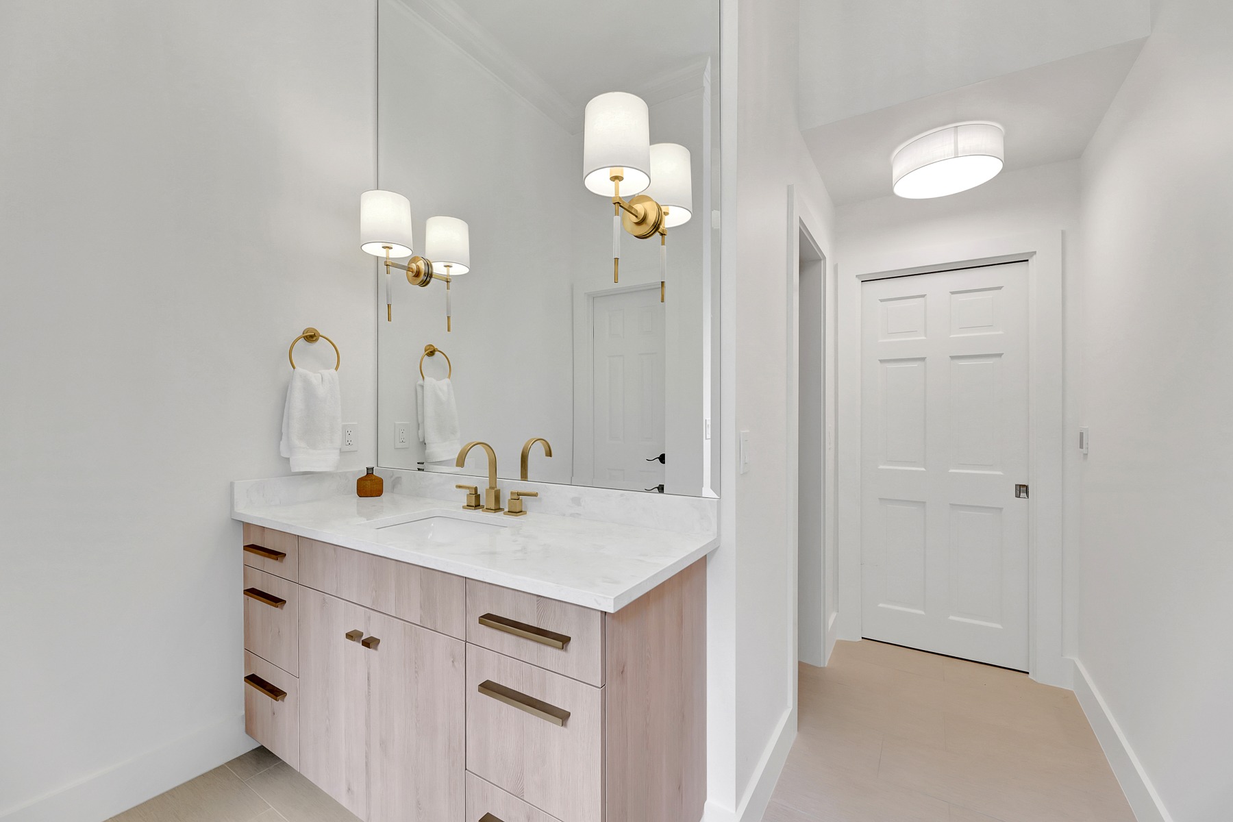 Modern bathroom with light wood cabinetry, white marble countertop, and stylish gold fixtures, featuring a large mirror and contemporary lighting, reflecting HomeVantage's design aesthetic for remodeling projects.