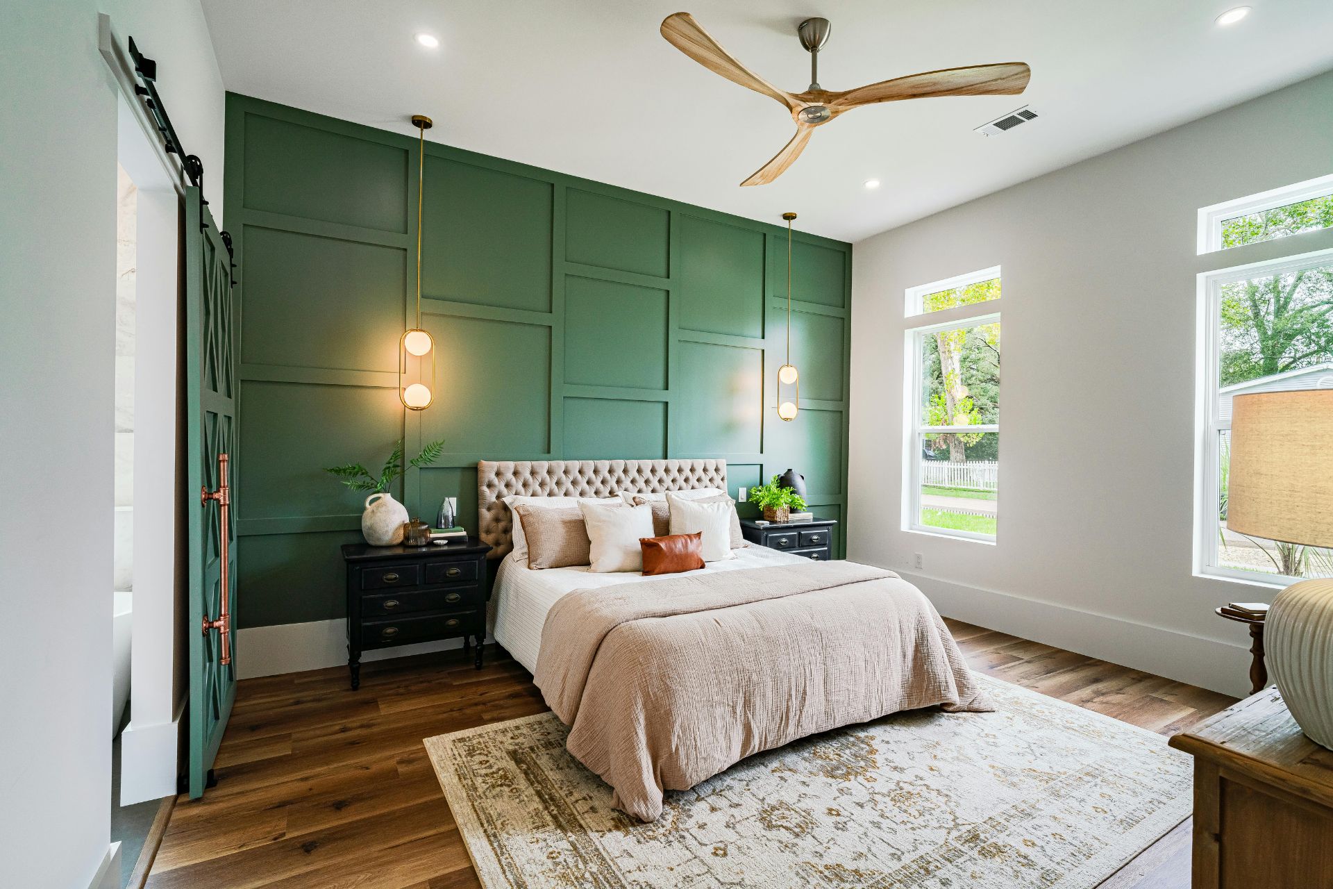 Bedroom interior featuring a green accent wall, a tufted headboard with decorative pillows, modern pendant lighting, and stylish furnishings, showcasing cohesive design elements for whole home remodeling.