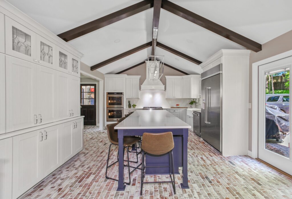 Modern kitchen design featuring white cabinetry, a large central island with seating, stainless steel appliances, and exposed wooden beams, showcasing a stylish and functional space for home renovations by HomeVantage.