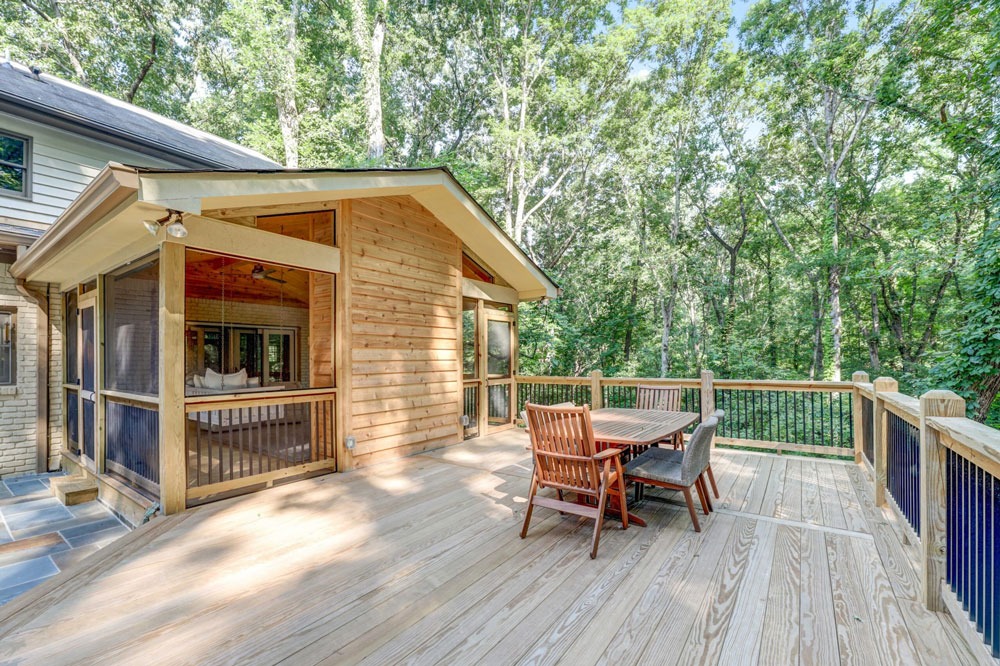 Outdoor deck renovation featuring wooden furniture and a screened-in porch, surrounded by lush greenery, showcasing HomeVantage's outdoor living project.