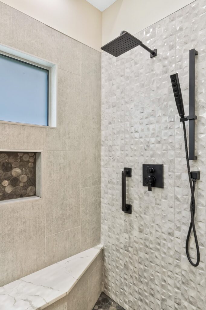 Modern bathroom shower featuring textured tile walls, a sleek black rain showerhead, hand shower, and a built-in stone accent niche, designed for HomeVantage renovation projects.