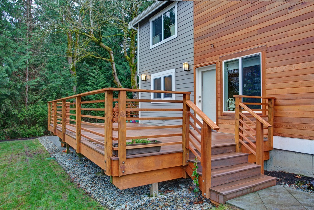 Wooden deck with railing and stairs leading to a modern home, surrounded by greenery, showcasing outdoor living space design by HomeVantage in North Metro Atlanta.