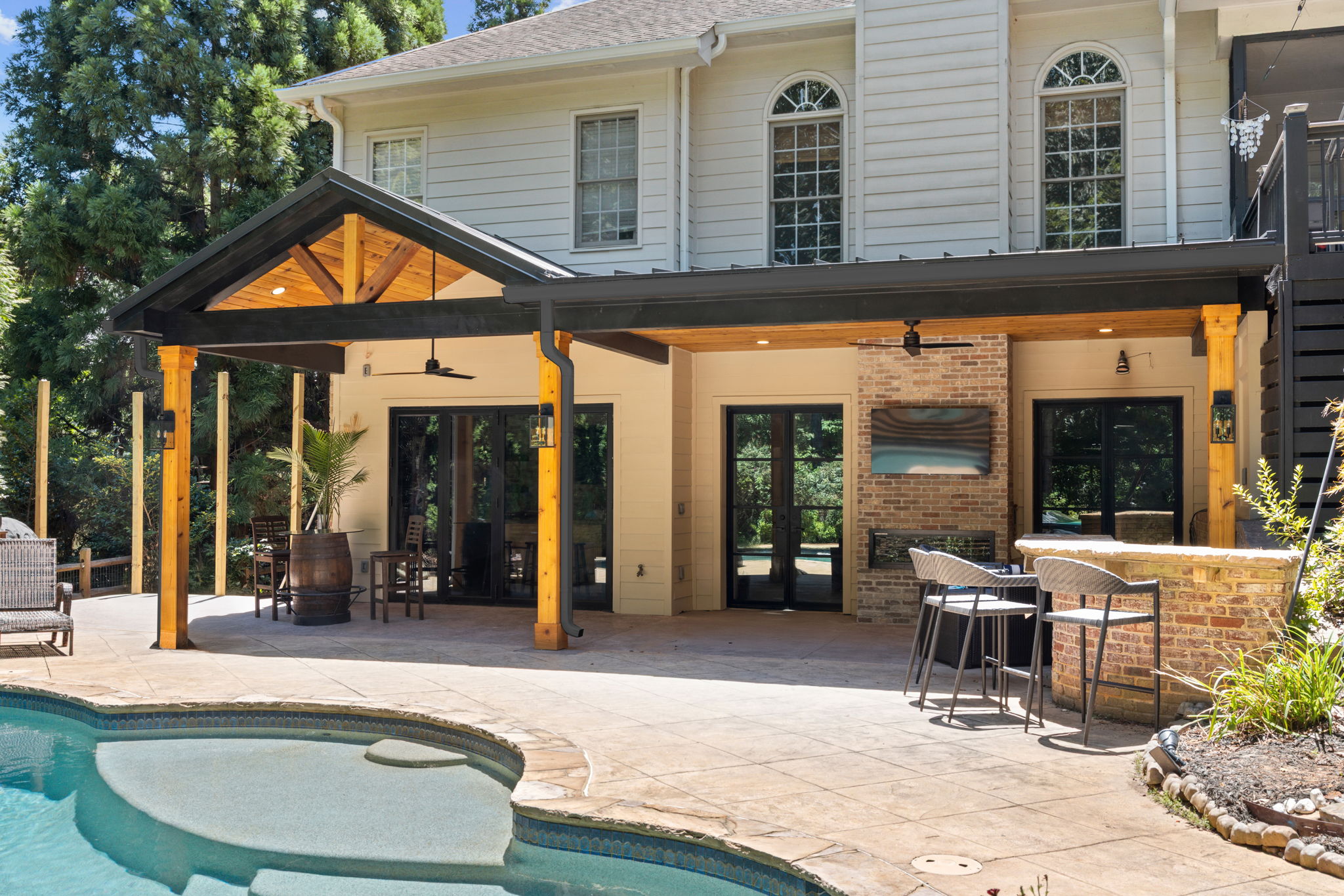 Outdoor living space featuring a covered patio with wooden beams, stylish bar seating, and a poolside view, designed for relaxation and entertaining.