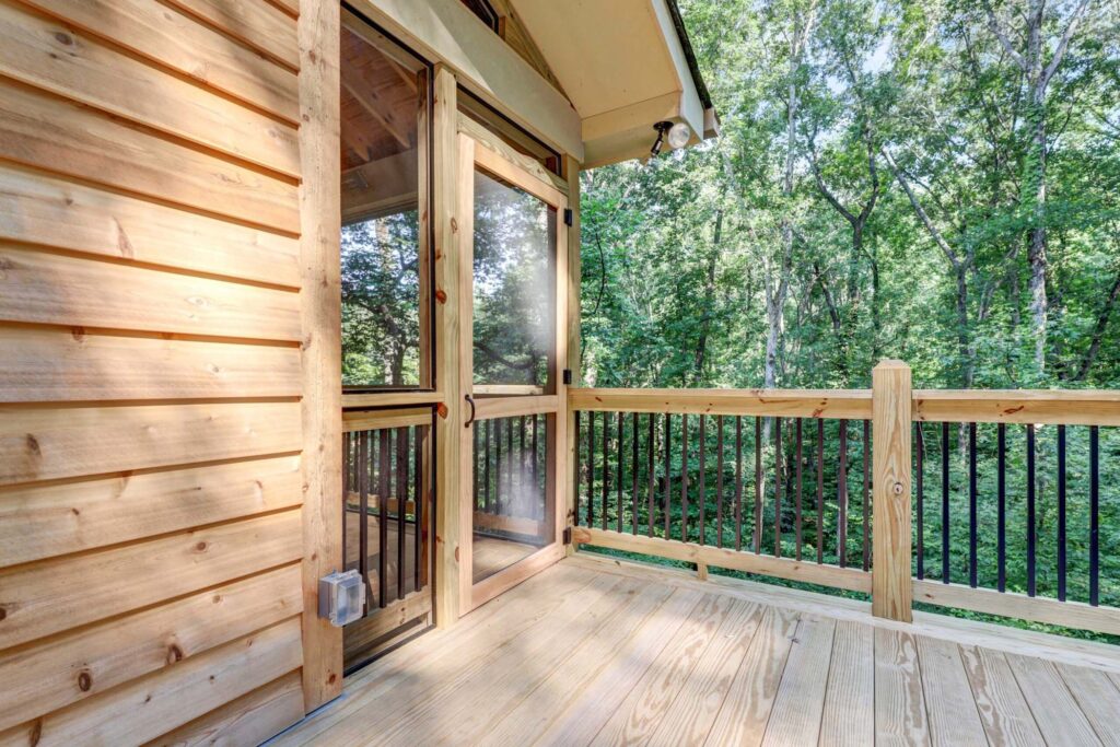 Custom screened-in porch with wooden framing and railing, showcasing a view of lush greenery, enhancing outdoor living space in a residential setting.