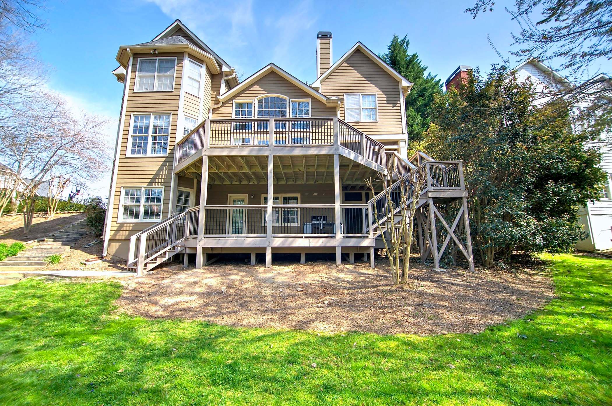Backyard view of a two-story home featuring a large, multi-level deck with railings, surrounded by green grass and shrubs, illustrating outdoor living space potential for HomeVantage projects in Metro Atlanta.