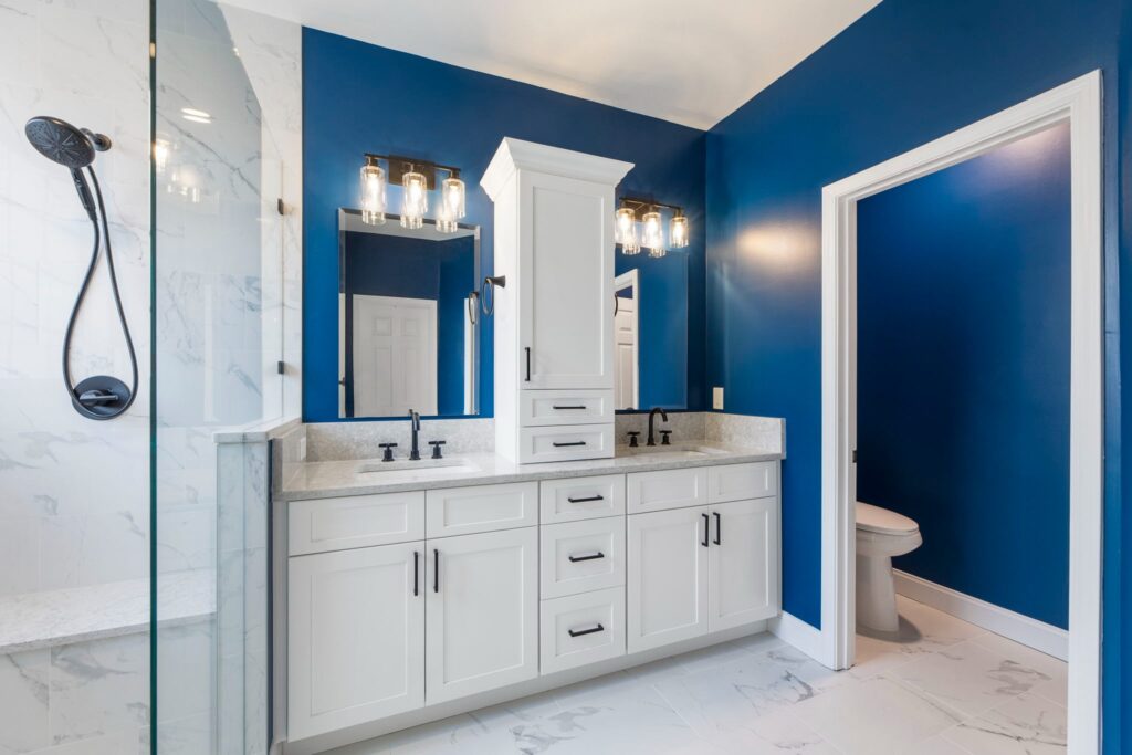 Modern bathroom with blue accent wall, white cabinetry, dual sinks, and glass shower, showcasing quality craftsmanship by HomeVantage in Alpharetta, GA.