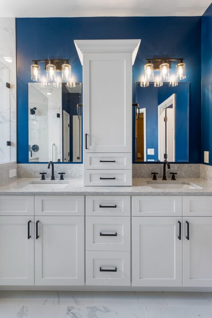 Modern bathroom design featuring dual sinks, white cabinetry, and navy blue accent wall with stylish lighting fixtures, showcasing HomeVantage's renovation expertise.