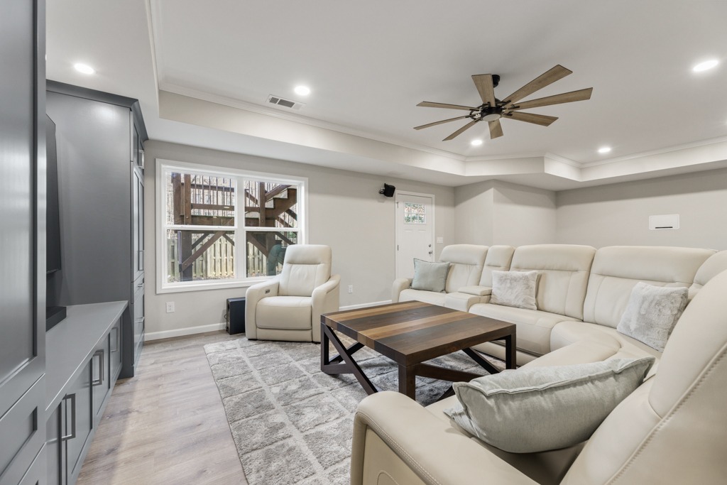 Modern basement living area featuring a light-colored sectional sofa, wooden coffee table, and large windows overlooking outdoor stairs, showcasing the Huddlestone basement remodeling project by HomeVantage in Cumming, GA.
