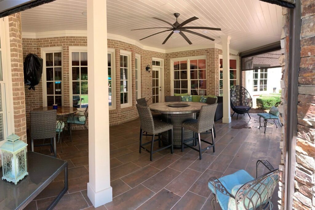 Outdoor living space featuring a covered patio with a large round table, wicker chairs, and stylish seating, showcasing HomeVantage's renovation expertise.