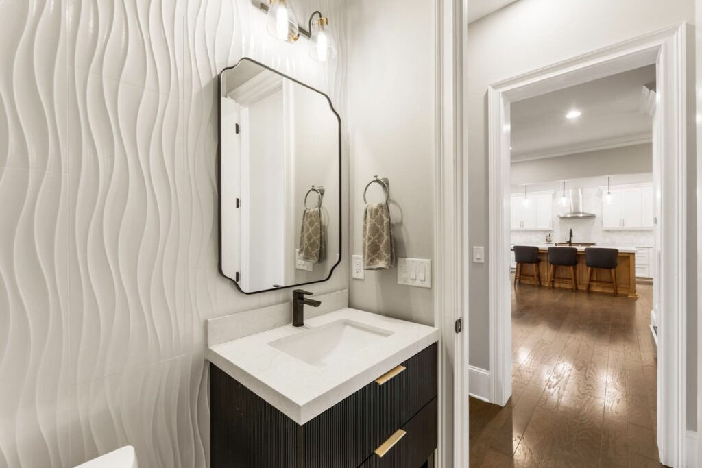 Modern bathroom design featuring a stylish black vanity with a white countertop, a decorative mirror, and textured wave-patterned wall, showcasing a contemporary aesthetic relevant to HomeVantage's bathroom renovation portfolio.