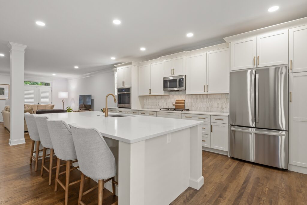 Modern kitchen with white cabinetry, stainless steel appliances, large island with seating, and hardwood flooring, showcasing design-first layout and premium craftsmanship for remodeling services in Alpharetta, GA.