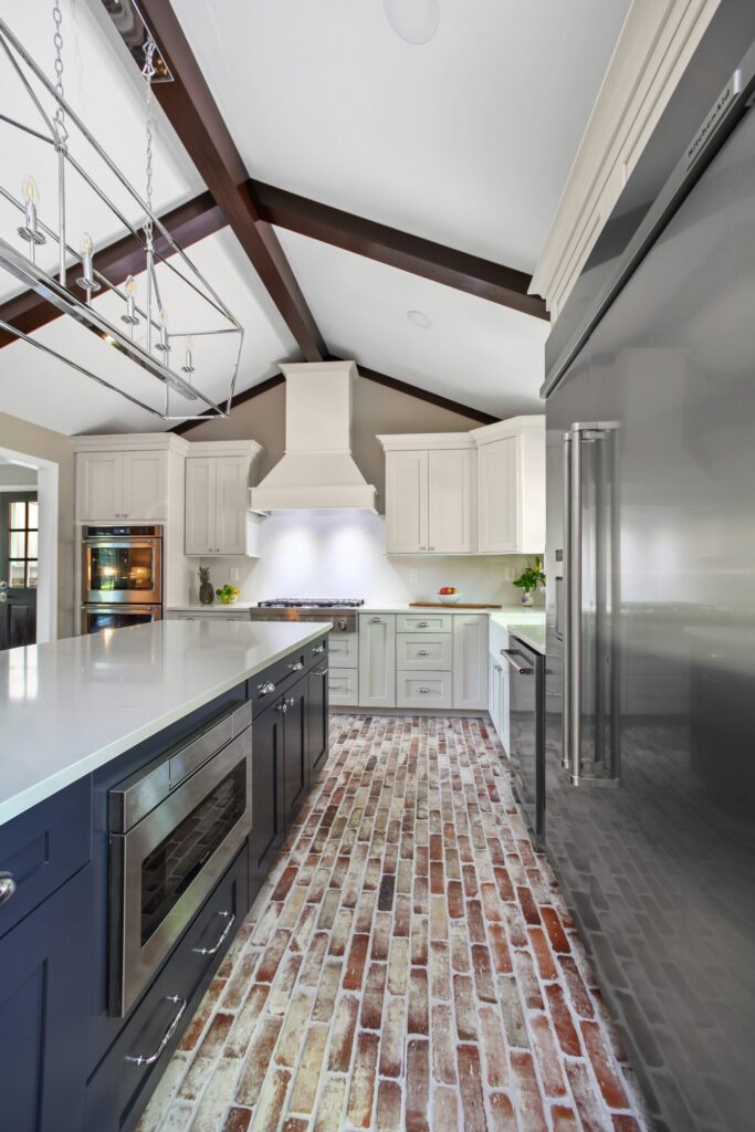 Modern kitchen remodel featuring dark cabinetry, white countertops, and exposed wooden beams, with a brick floor and stainless steel appliances, showcasing high-quality craftsmanship.