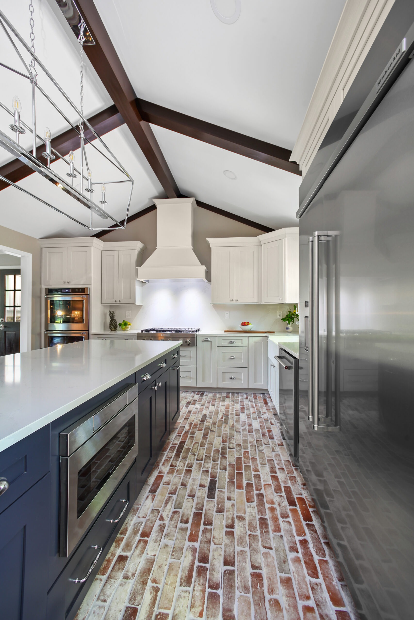 Modern kitchen design featuring a spacious island with dark cabinetry, light countertops, and a brick-patterned floor, complemented by recessed and pendant lighting, showcasing premium craftsmanship and a stylish atmosphere.