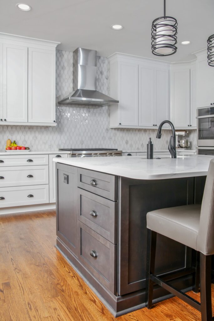 Modern kitchen with white cabinetry, marble countertop, stainless steel hood, and dark island featuring drawers, showcasing a blend of functionality and design in a Cumming, GA home remodel.