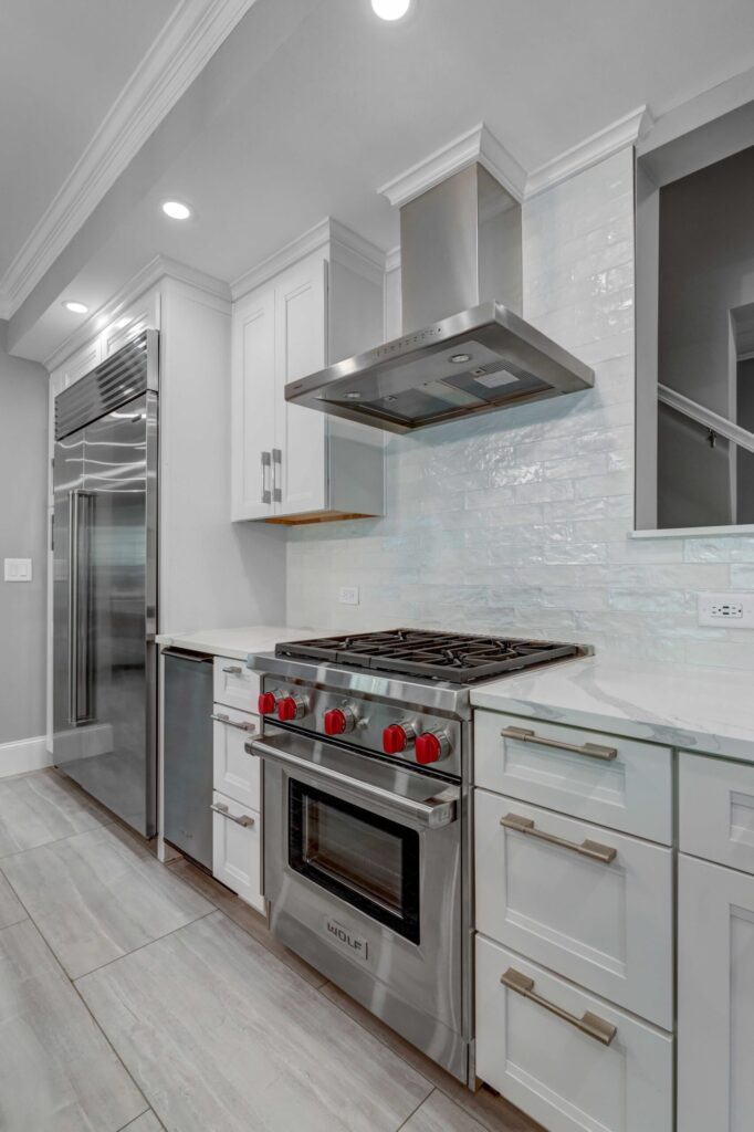 Modern kitchen design featuring stainless steel Wolf range with red knobs, sleek white cabinetry, and stylish backsplash, emphasizing premium craftsmanship and functional layout.