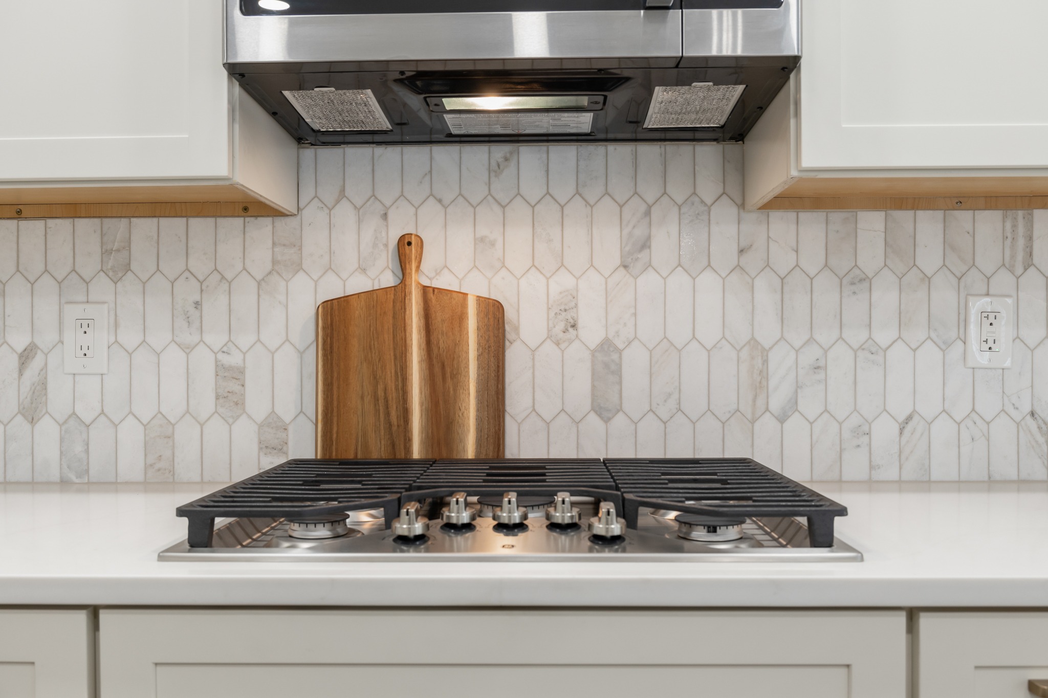 Modern kitchen design featuring a sleek gas stovetop, elegant hexagonal tile backsplash, and a wooden cutting board, illustrating premium craftsmanship and functional layout for cooking and everyday living.