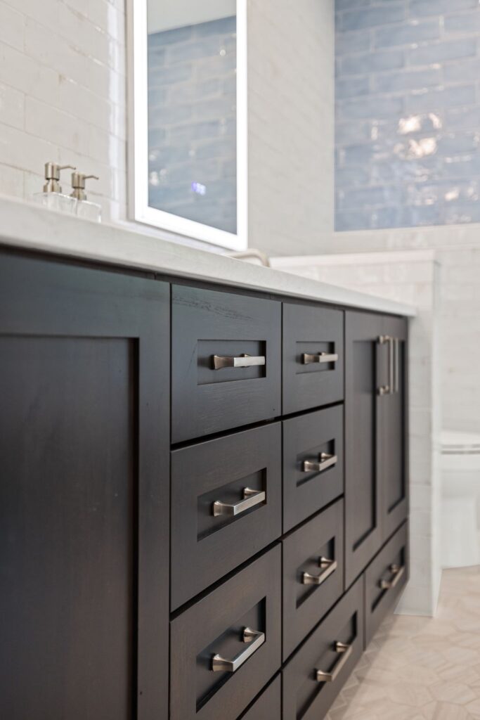 Bathroom vanity with dark cabinetry, modern handles, and a mirror reflecting light, featuring a blue tiled wall in the background, showcasing HomeVantage's bathroom remodeling project on Oakhaven Drive, Roswell, GA.