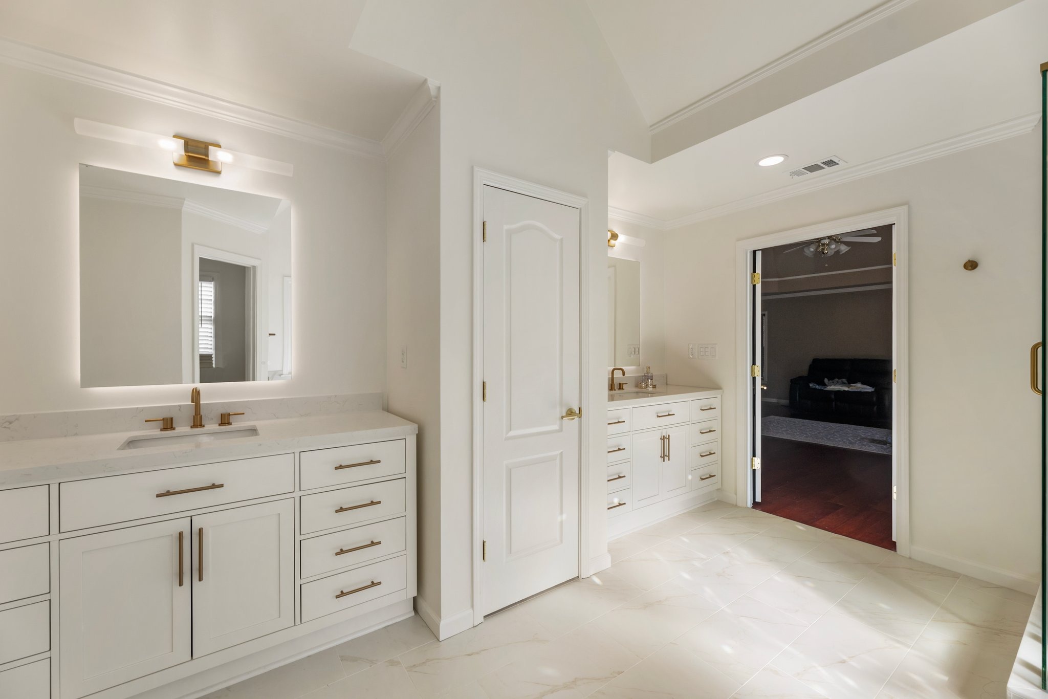 Modern bathroom interior featuring dual vanities with gold fixtures, white cabinetry, and a well-lit mirror, showcasing a clean and organized space ideal for home remodeling projects.