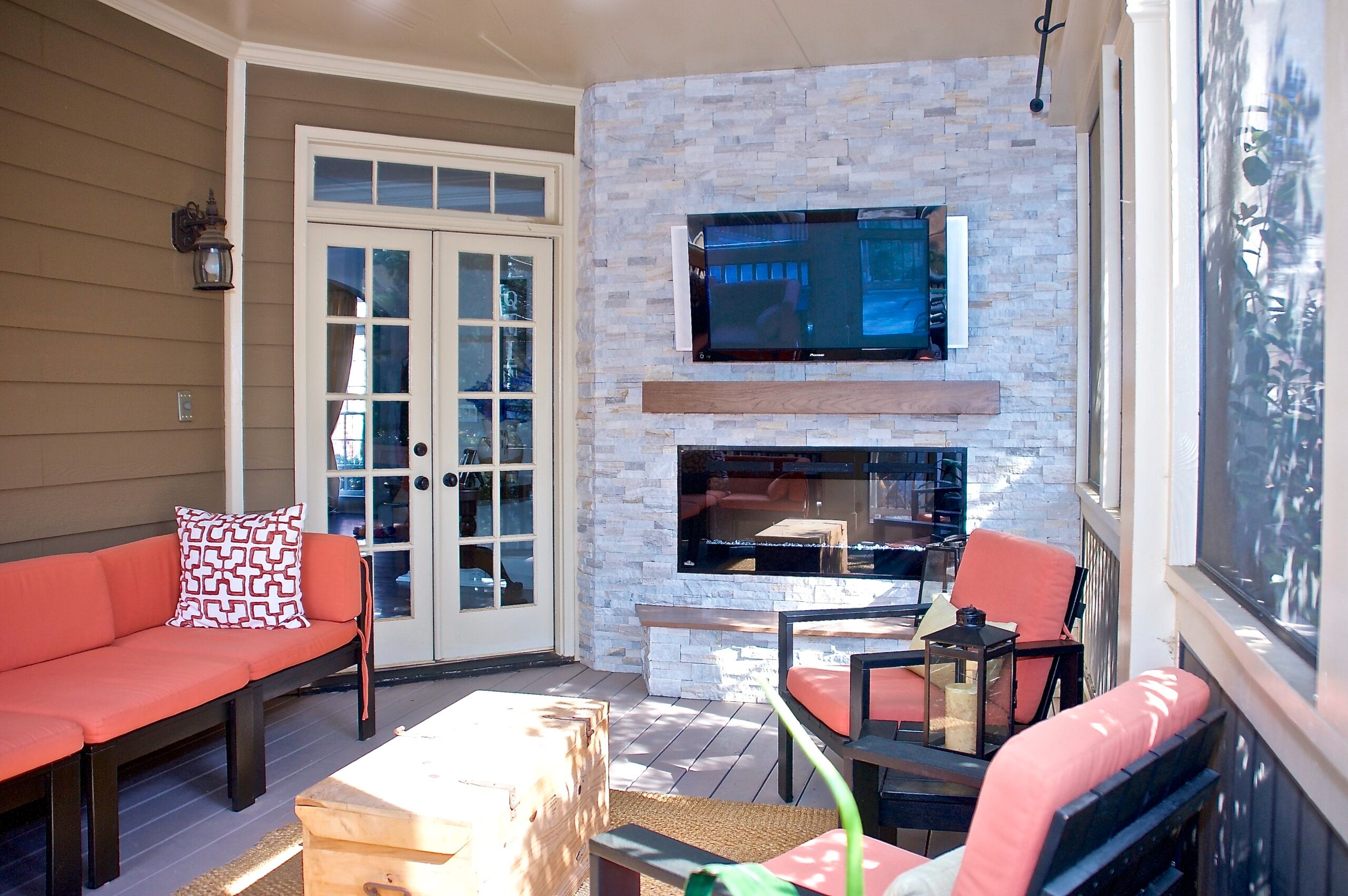 Outdoor living space featuring modern seating, stone fireplace, and wall-mounted TV, designed for comfort and relaxation in home renovations.