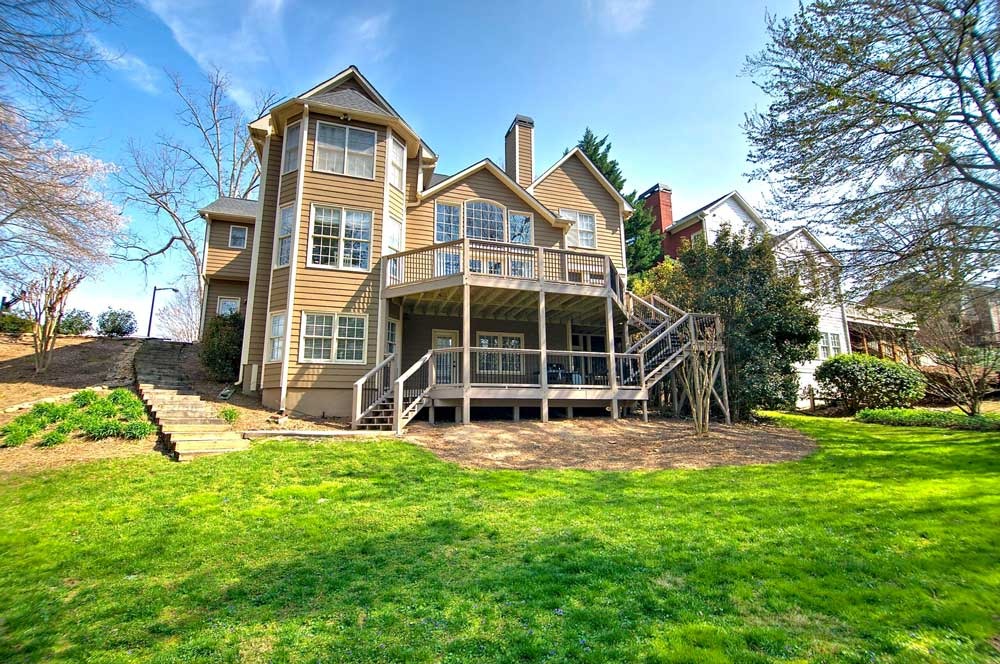 Outdoor renovation of a spacious home with a large deck, surrounded by greenery and steps leading to the backyard.