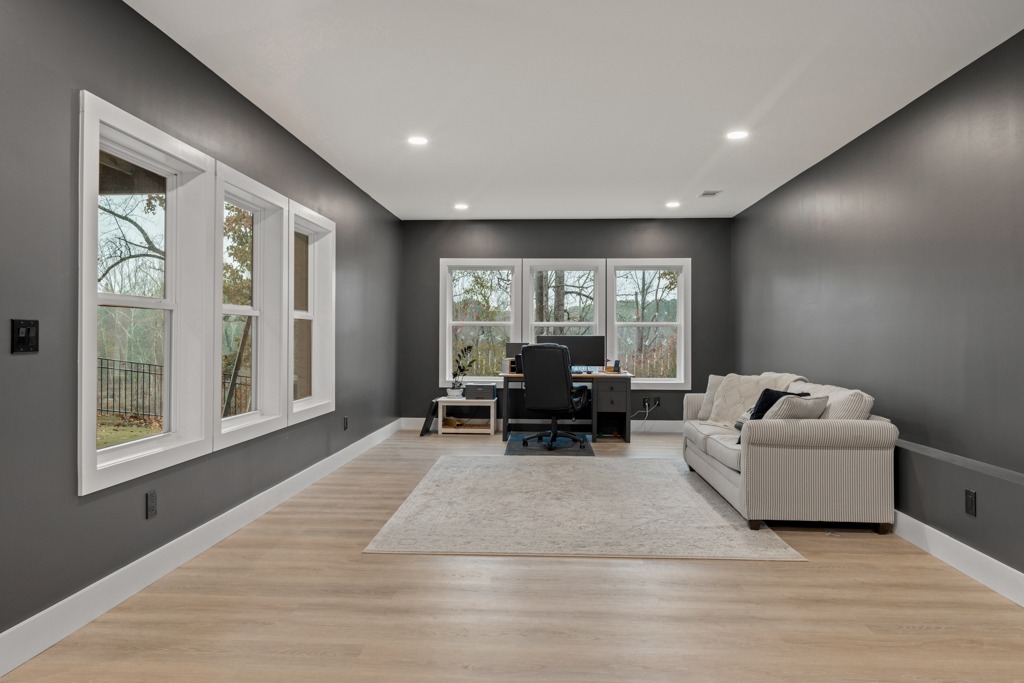 Modern home office space with gray walls, large windows, a comfortable sofa, and a desk area featuring a computer, emphasizing the transformation potential in residential remodeling.