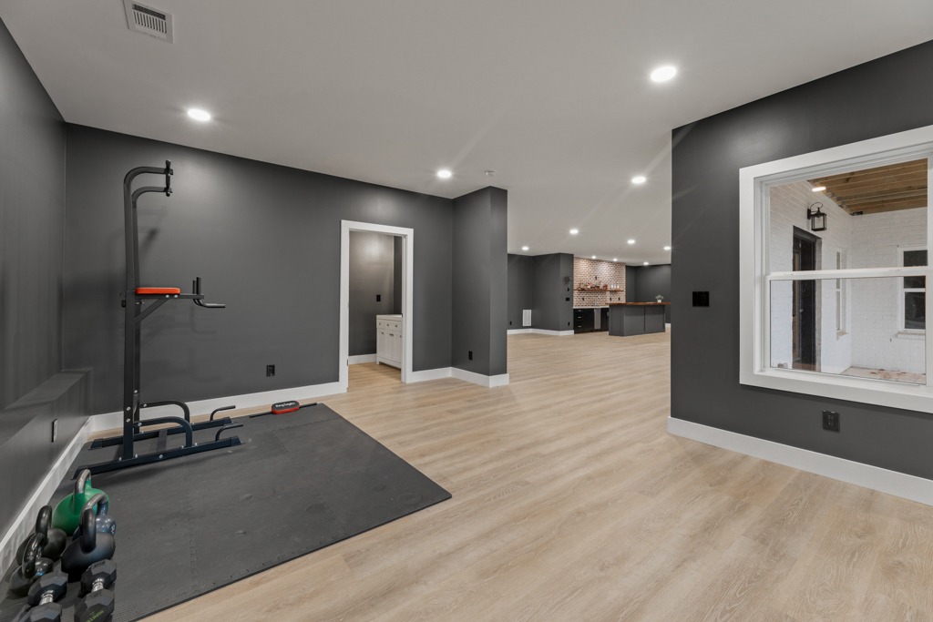 Modern home gym space featuring a pull-up bar, free weights, and sleek gray walls, showcasing a seamless transition to a renovated living area with hardwood flooring and ample lighting, reflecting HomeVantage's commitment to quality renovation.