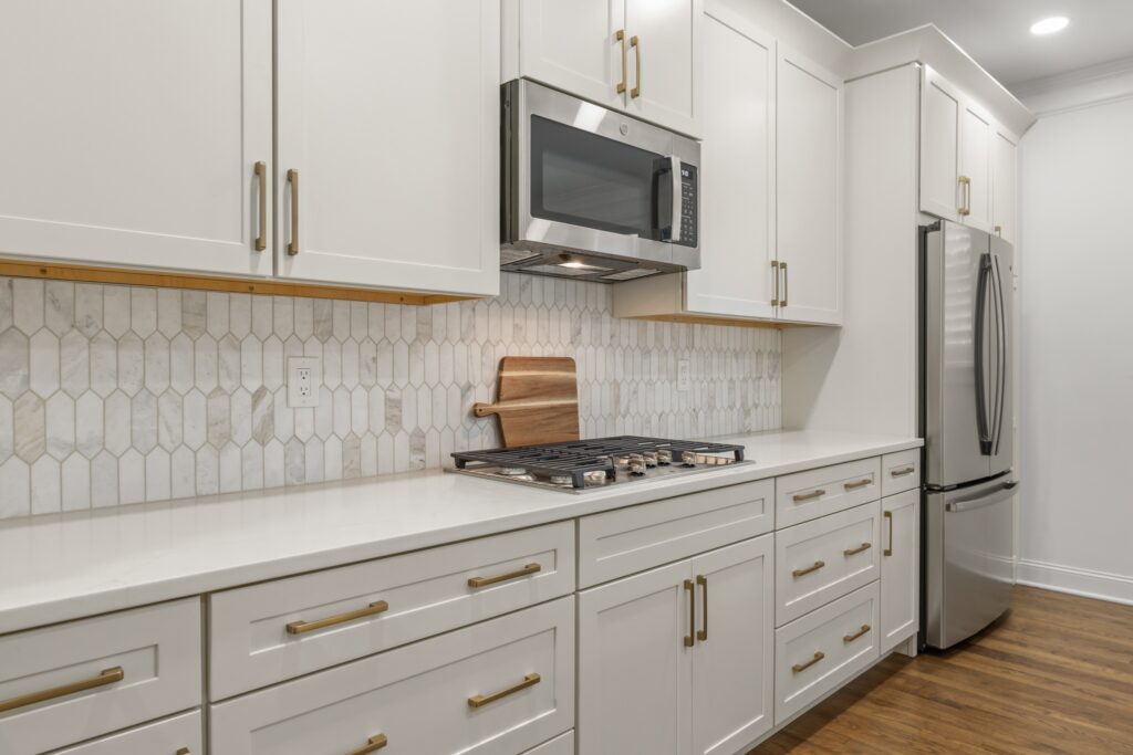 Modern kitchen renovation featuring white cabinetry, hexagonal tile backsplash, stainless steel appliances, and a gas stove, emphasizing design consistency and functionality in whole home remodeling.