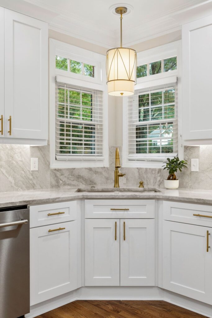 Modern kitchen corner with white cabinetry, gold hardware, marble countertops, and a stylish pendant light, showcasing a functional and aesthetically pleasing design ideal for home remodeling.