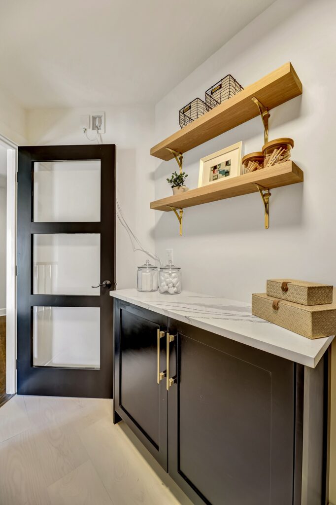 Modern bathroom interior featuring sleek black cabinetry, marble countertop, and open wooden shelves with decorative items, emphasizing contemporary design for home renovations.