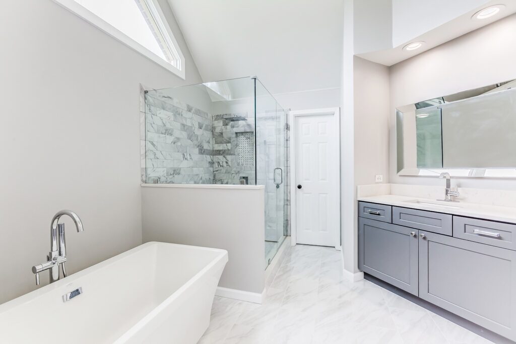 Modern bathroom design featuring a freestanding tub, glass shower enclosure, marble tile accents, and sleek gray cabinetry, showcasing HomeVantage's renovation expertise.